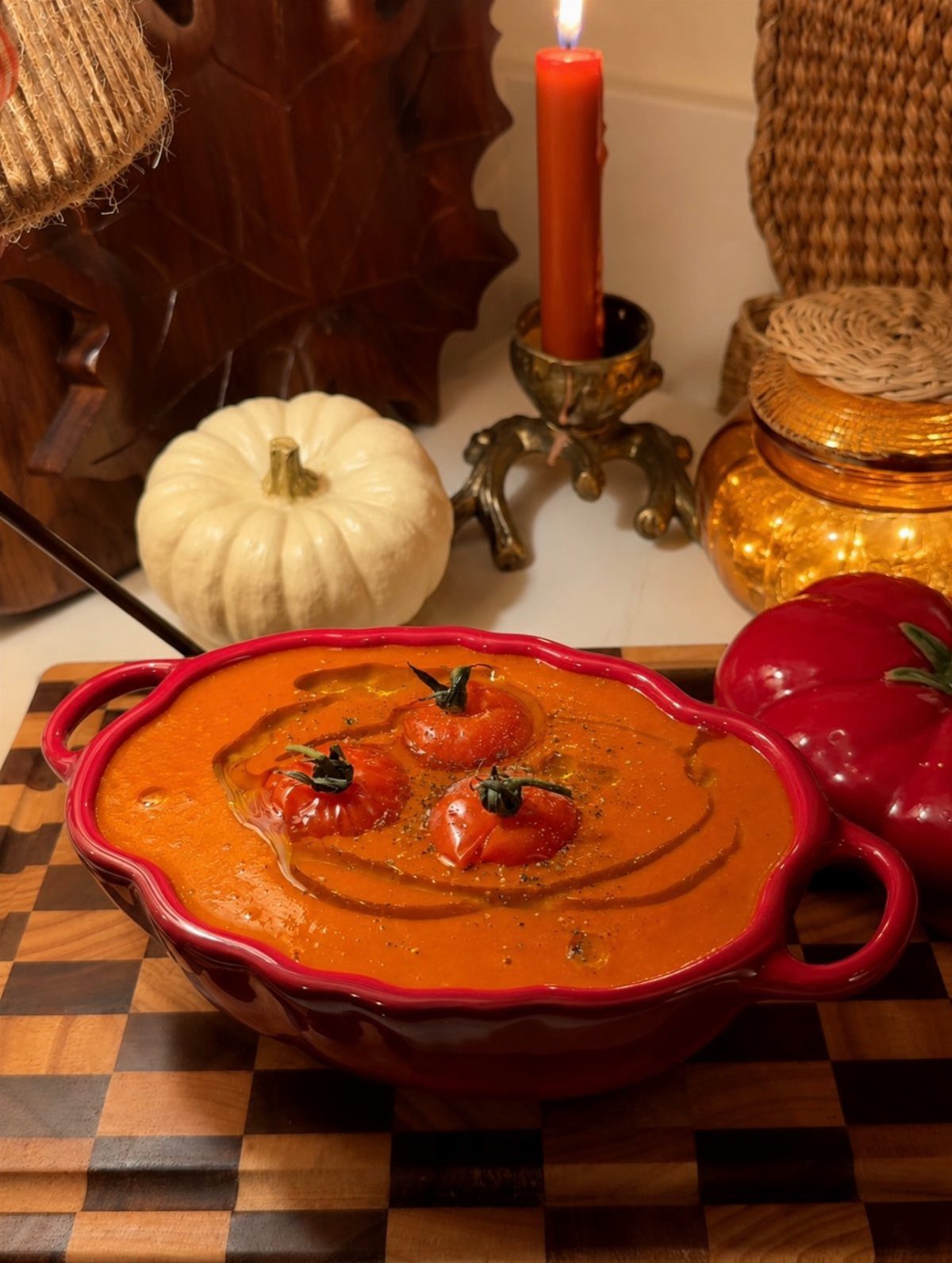 Tomato soup in a red bowl topped with roasted tomatoes on a wooden board.