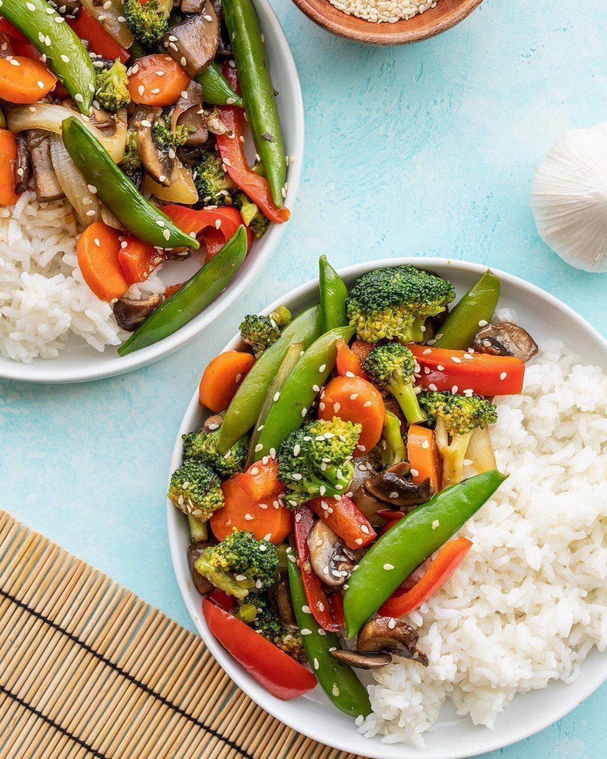 Two bowls of vegetable stir-fry with broccoli, carrots, and snap peas served over white rice.