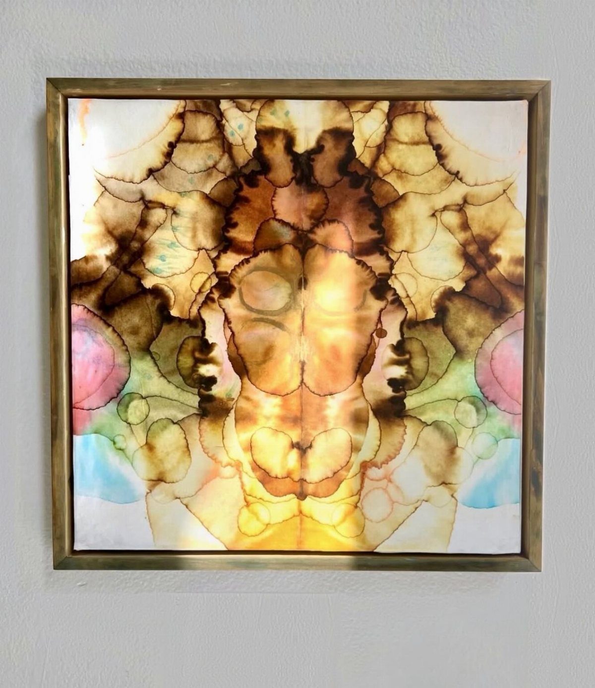 Abstract watercolor painting in a gold frame hanging on a light gray wall.