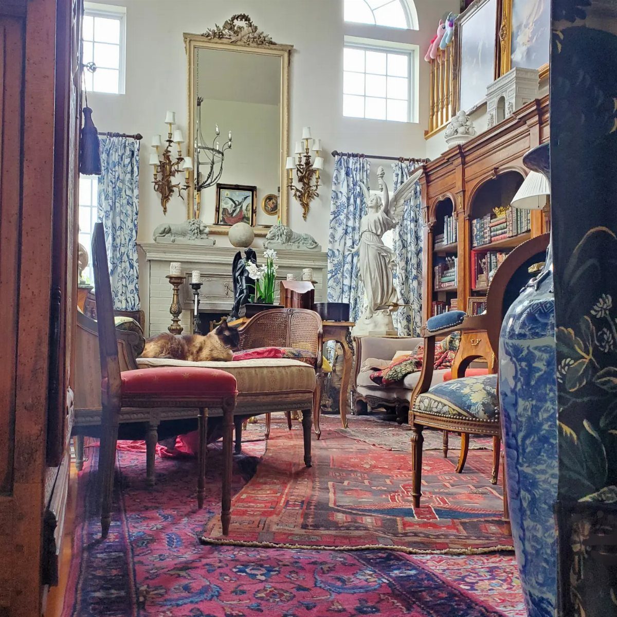 Antique furniture and patterned rugs layered across a living room floor with a cat resting on a bench.