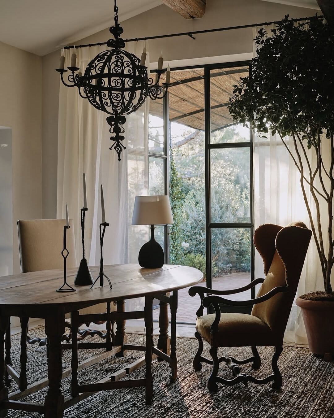 Dark wood dining table with mismatched chairs and a black wrought iron chandelier near glass doors.