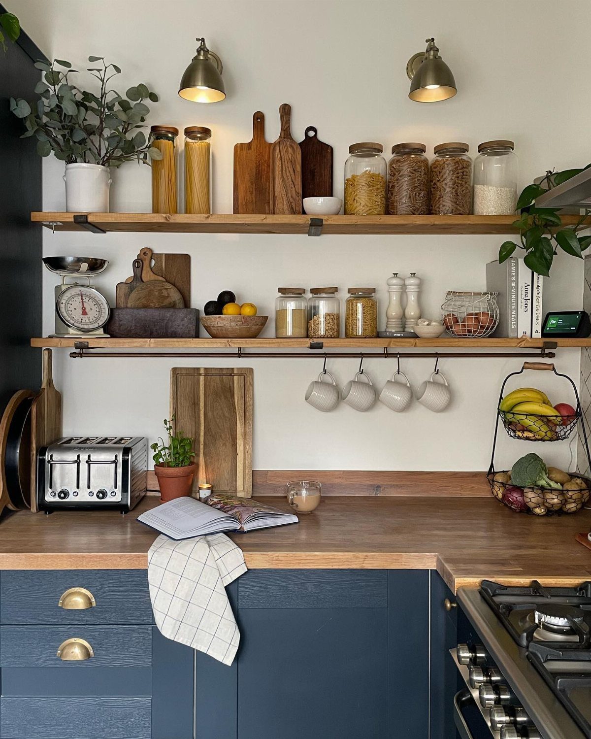 Wooden open shelves displaying glass jars, cutting boards, and kitchenware against a white wall.
