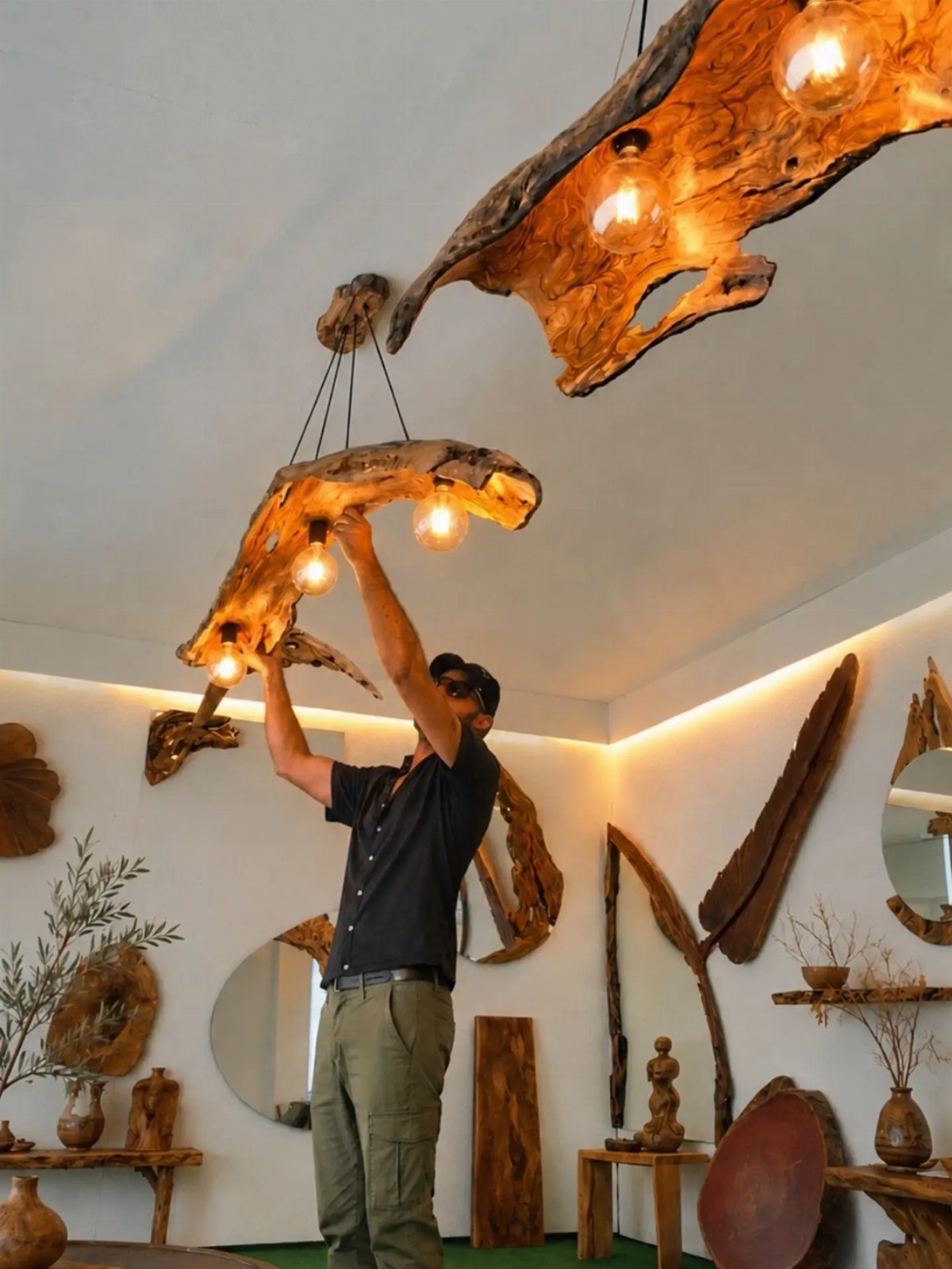 A man adjusting a large rustic wooden slab light fixture with glowing bulbs on a white ceiling.