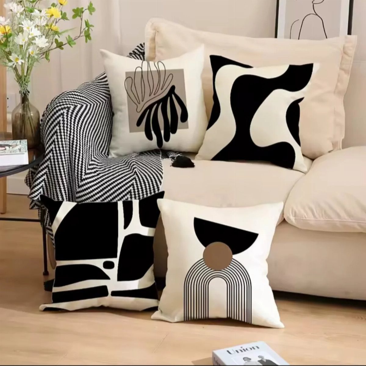 Four abstract patterned pillows in black and cream resting on a neutral colored sofa.