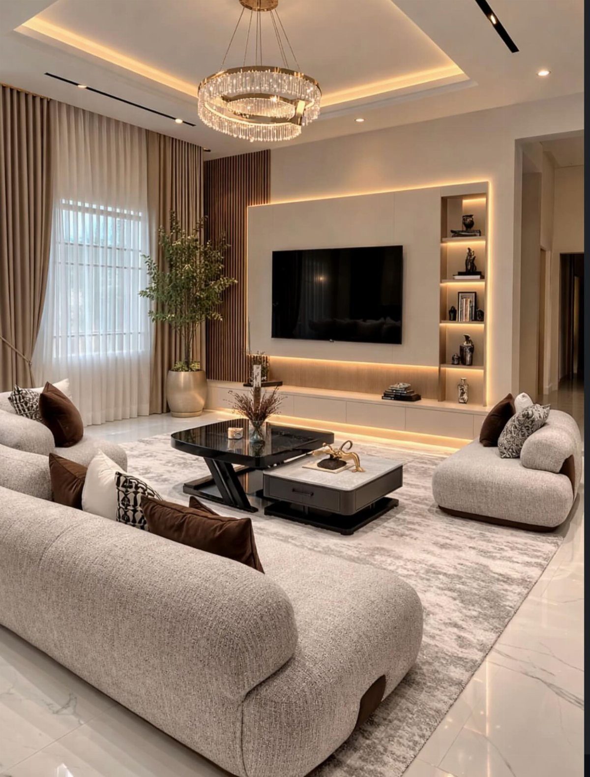 A crystal chandelier hangs above a modern living room with neutral furniture and warm lighting.