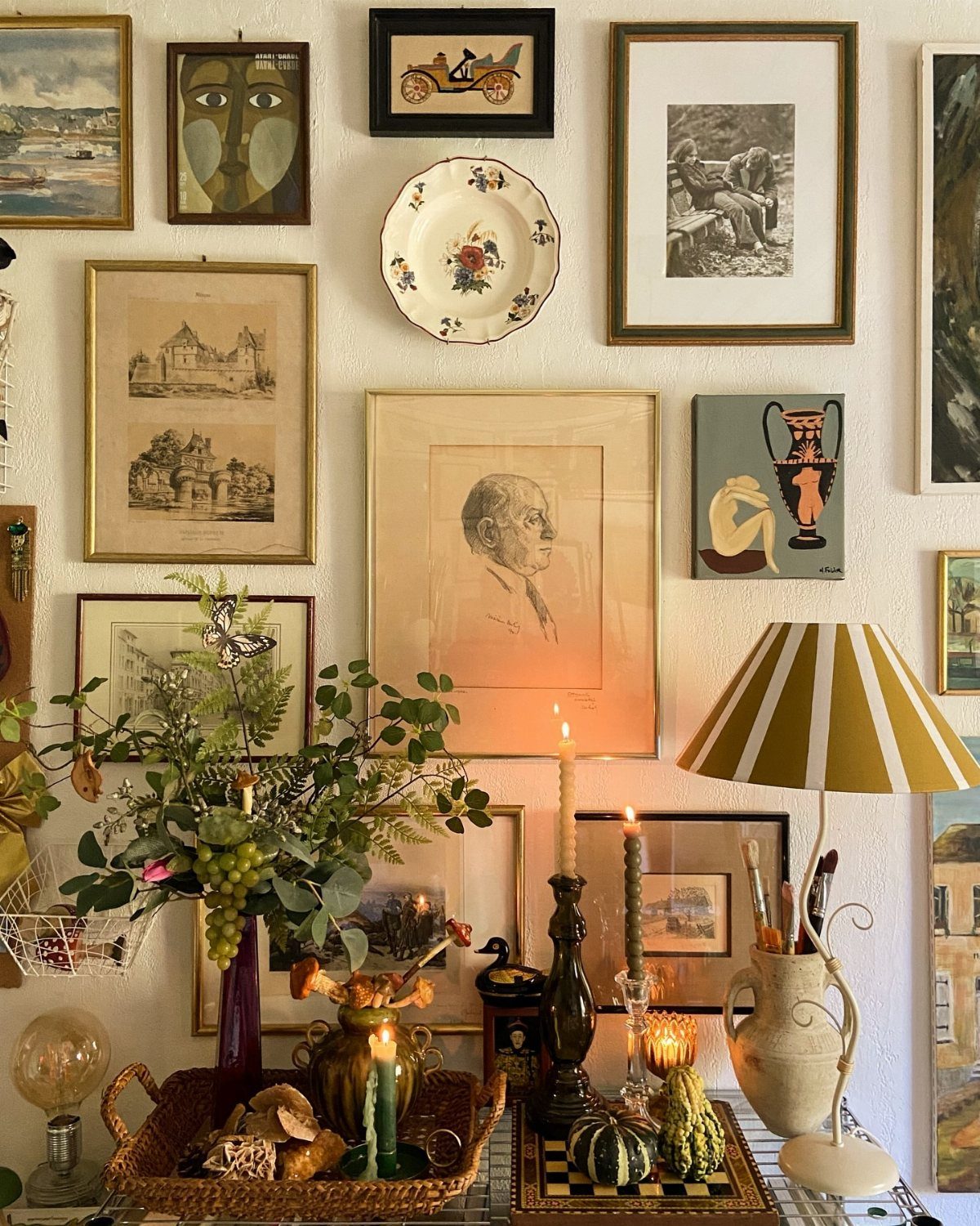 A gallery wall with framed art, a decorative plate, and a table with candles and greenery.