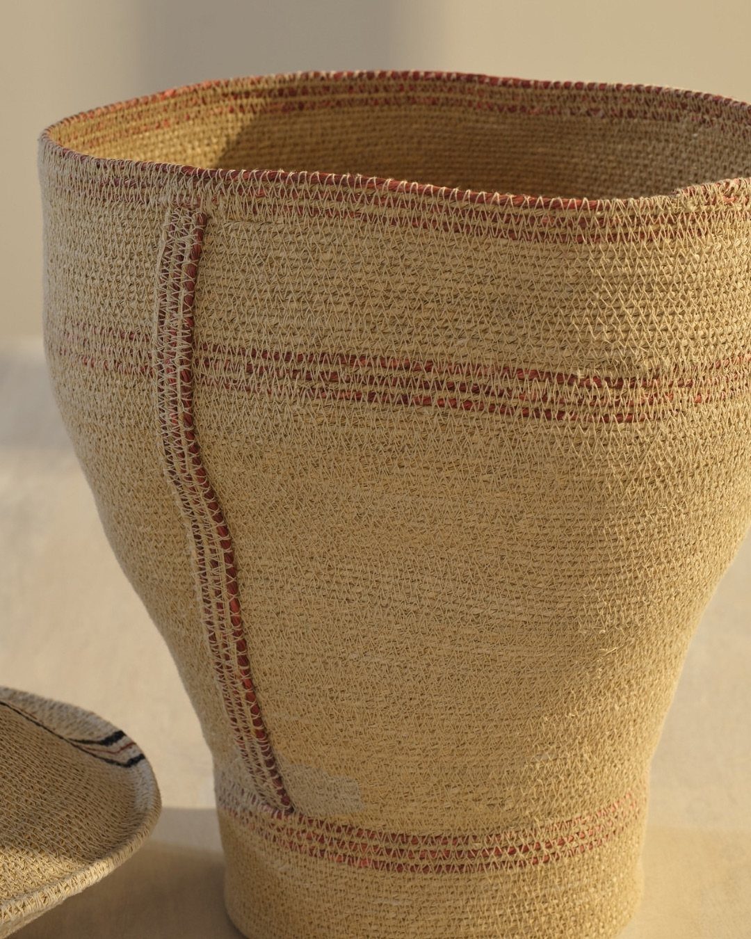 A close-up of a beige woven basket with red stripes and a matching lid.