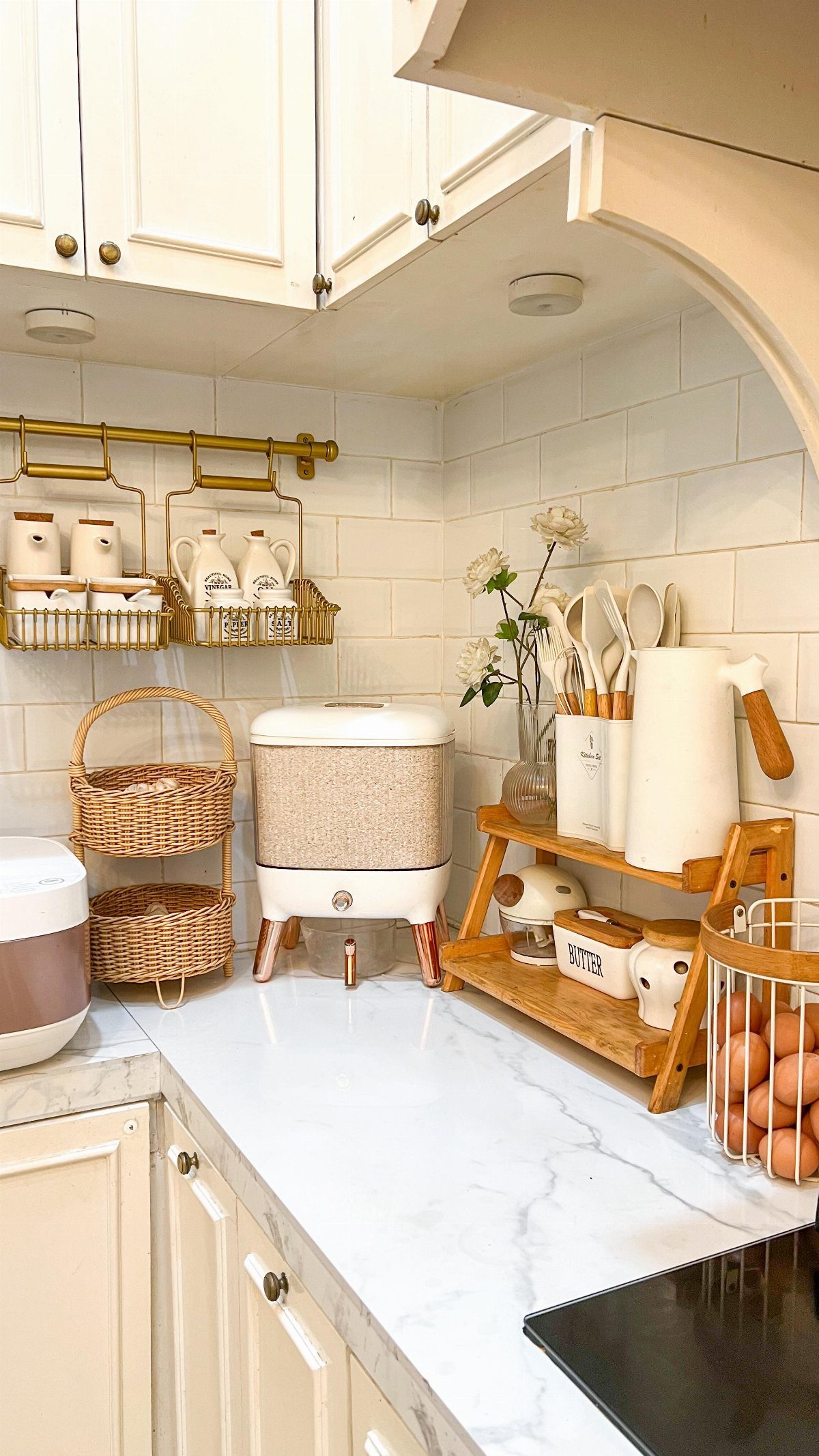 Wicker baskets and wooden organizers sit on a white marble kitchen countertop against subway tiles.