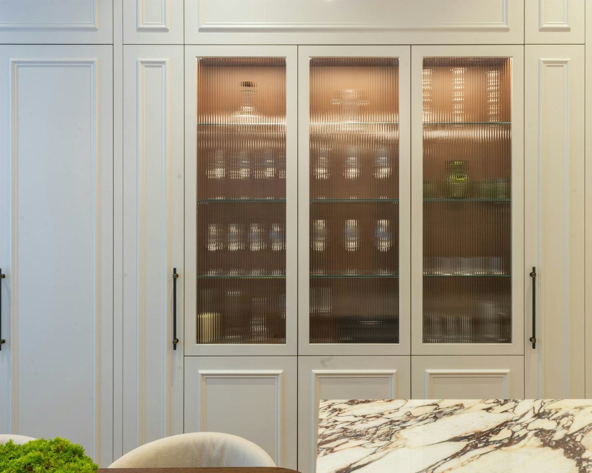 White ribbed glass-front kitchen cabinets displaying various glassware on illuminated interior shelves.