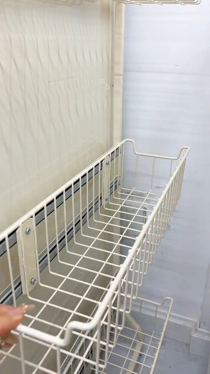 A hand adjusting a white wire basket mounted on a sliding rail inside a refrigerator.