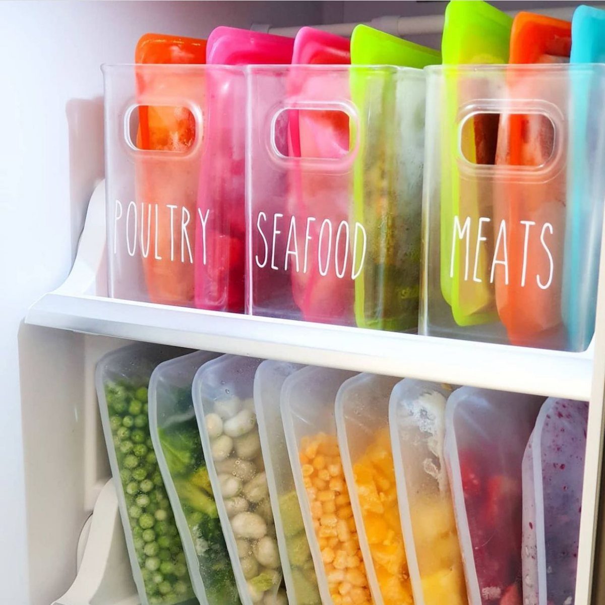 Clear refrigerator bins labeled Poultry, Seafood, and Meats containing colorful silicone storage bags.