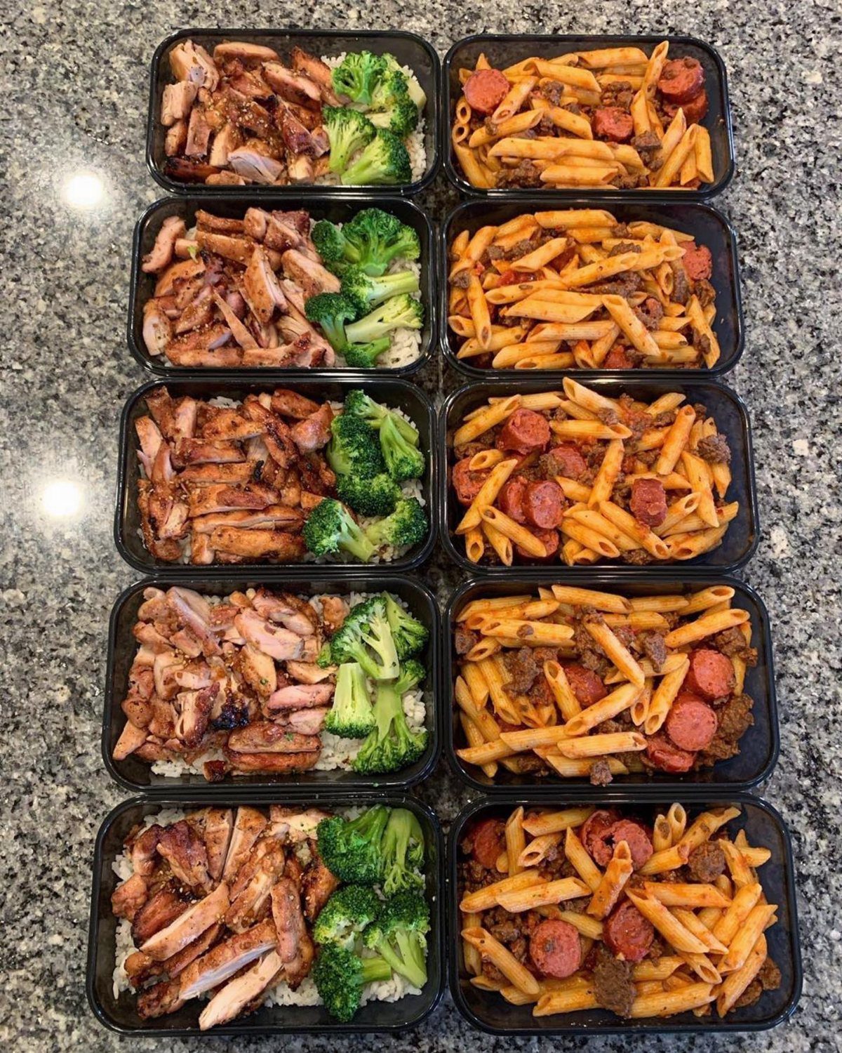 Ten black containers filled with prepared chicken and broccoli or pasta meals on granite.