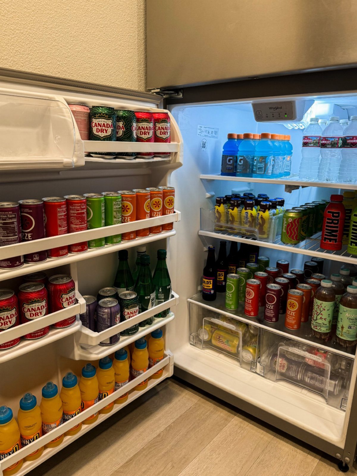 An open refrigerator door filled with neatly organized rows of colorful canned and bottled beverages.