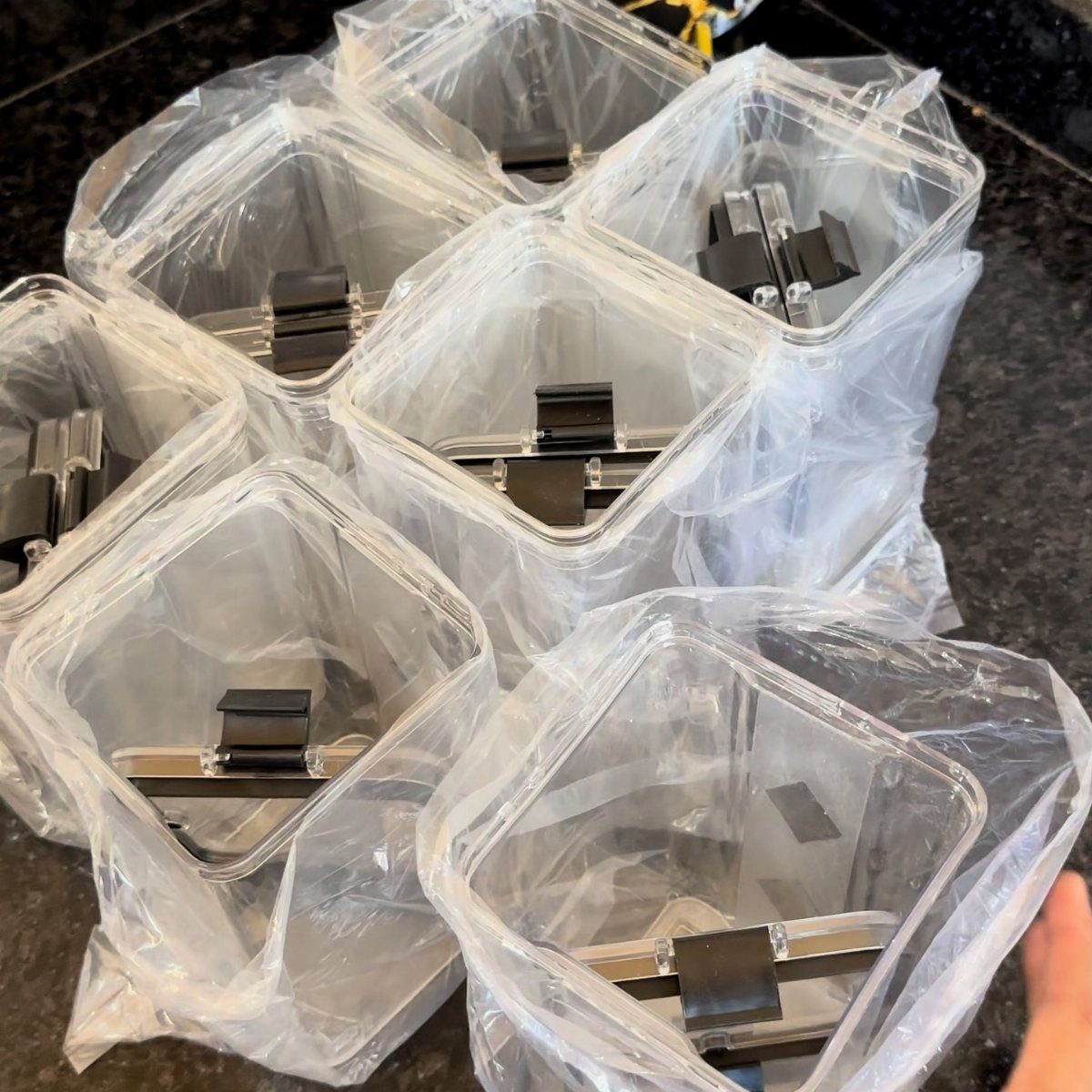 Clear plastic storage containers with black handles clustered on a dark countertop.