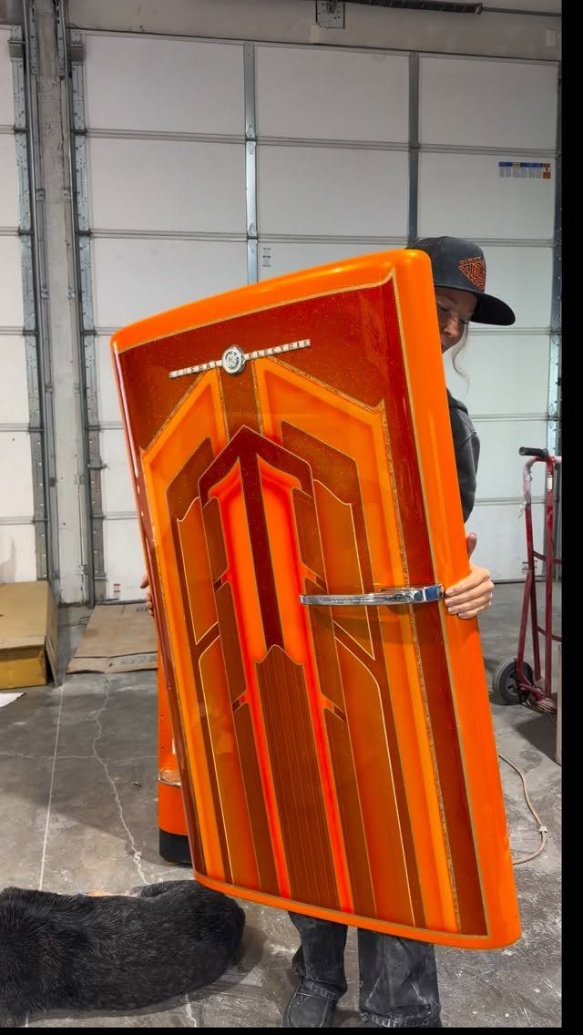 A person holding an orange refrigerator door with a retro geometric design.