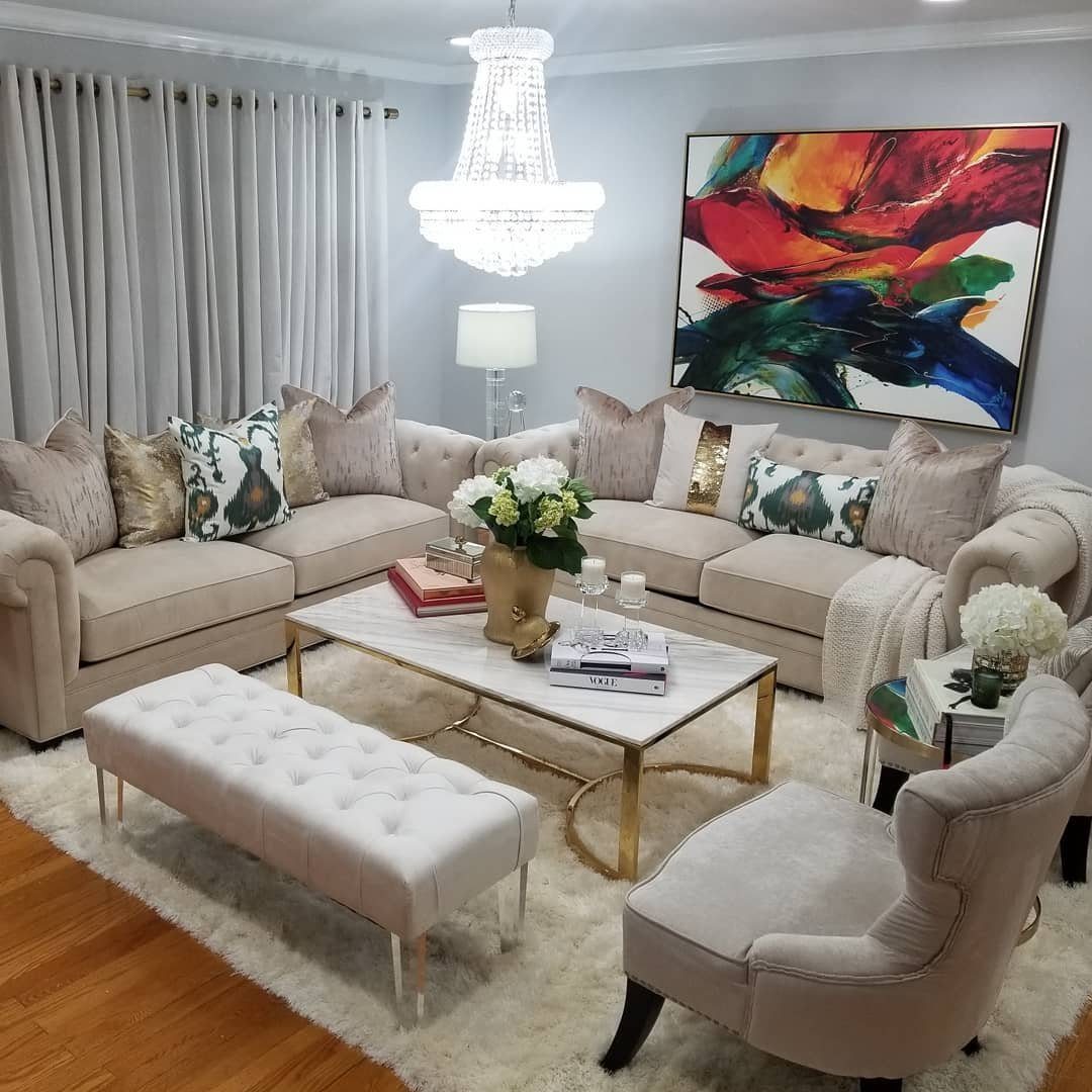 Beige sectional sofa with decorative pillows arranged around a marble coffee table on a white shag rug.