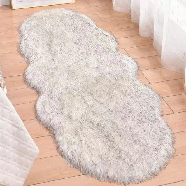 A light grey faux fur rug resting on a light wooden floor near white curtains.