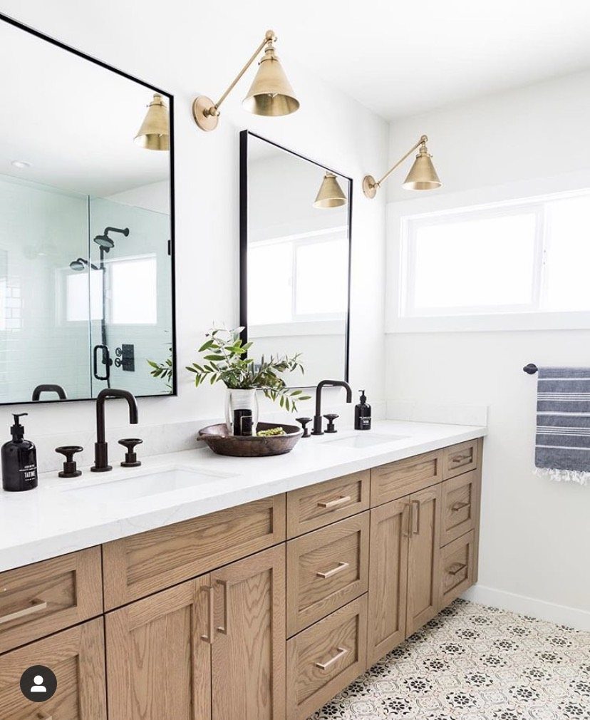 Black faucets and gold wall sconces installed on a white bathroom vanity.