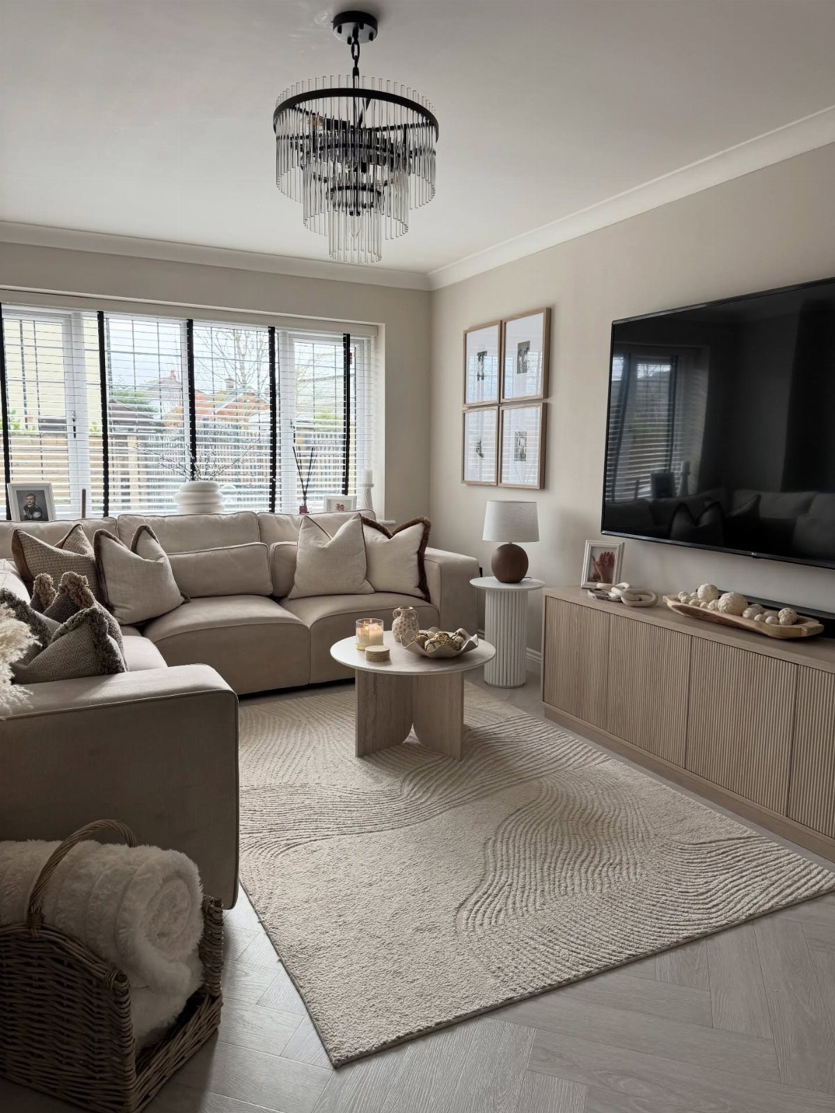 Beige living room furniture with a large crystal chandelier and textured rug.