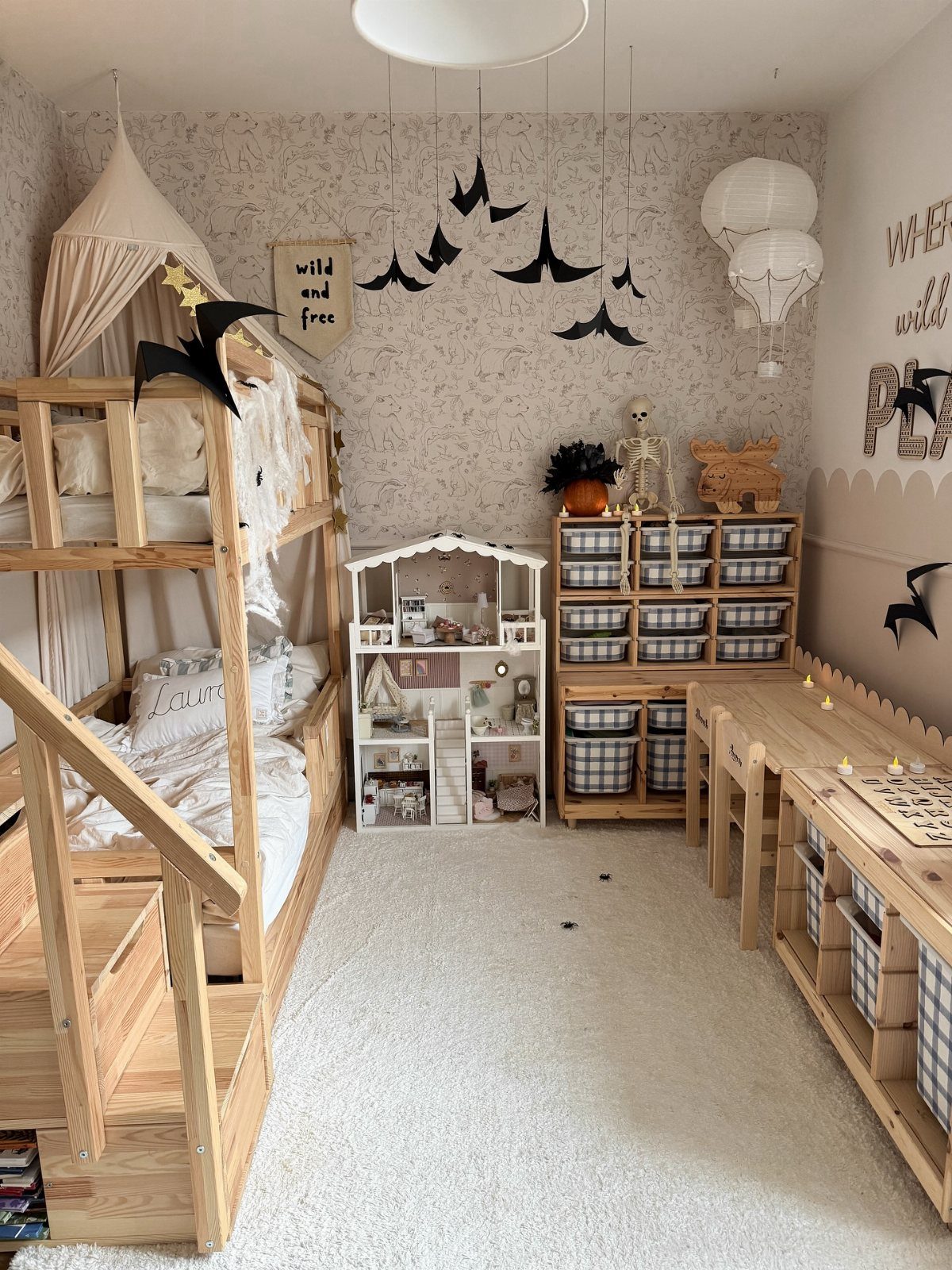 A child's bedroom with wooden bunk beds, a dollhouse, and black bat decorations hanging from the ceiling.