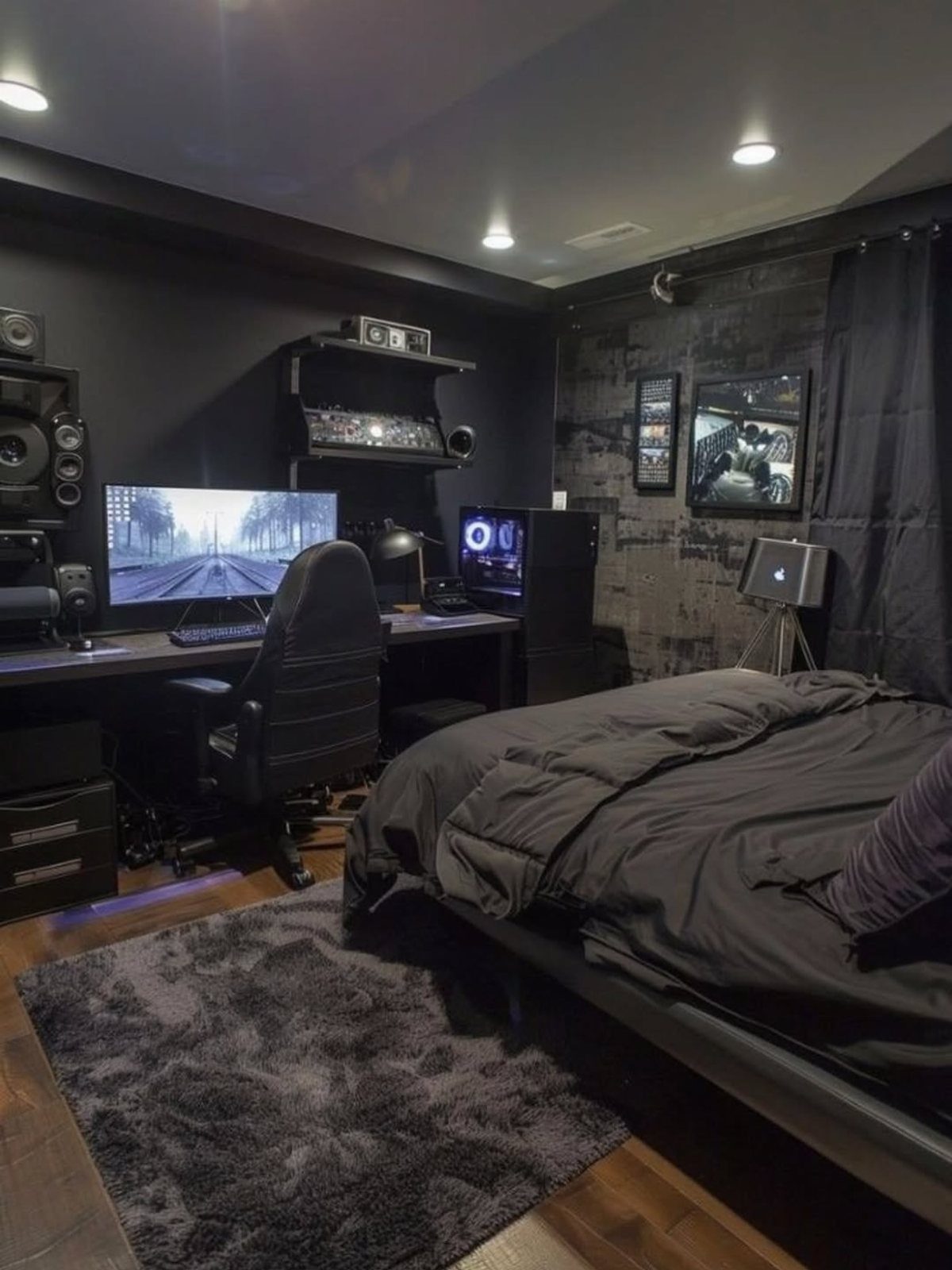 A dark bedroom with black walls, a computer desk, and a bed with black bedding.