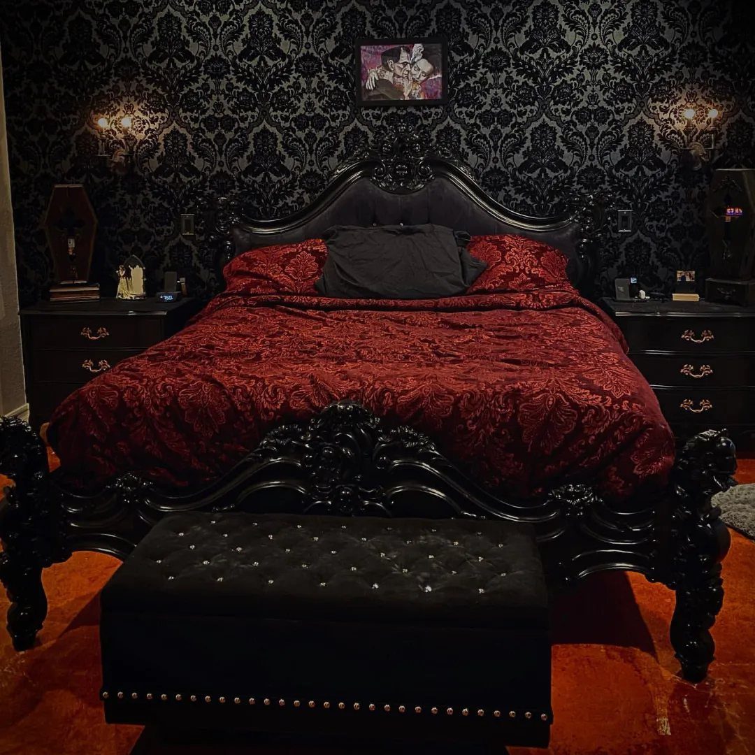 Ornate black bed with red bedding against black damask patterned wallpaper in a gothic bedroom.