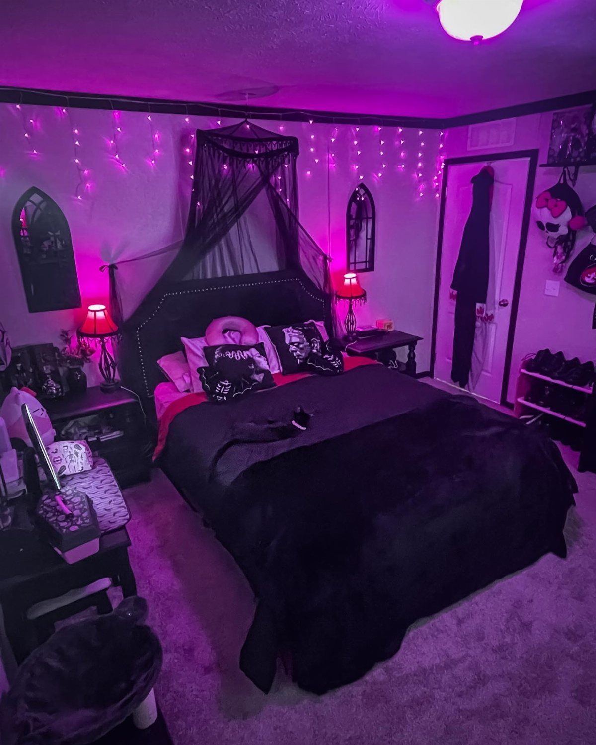 A gothic teen bedroom featuring black bedding, a canopy, and vibrant pink string lights.