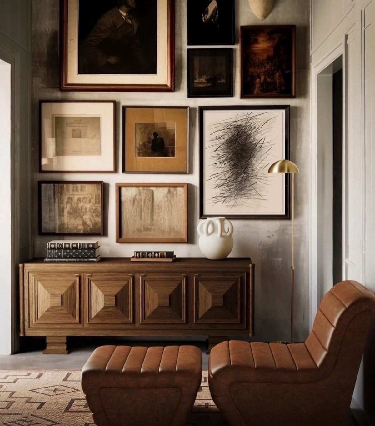 A collection of framed art pieces arranged on a grey-green wall above a wooden sideboard.