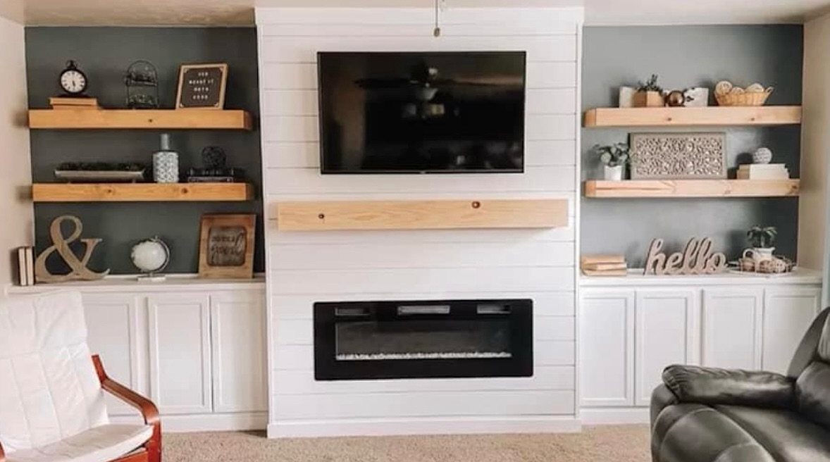 White shiplap fireplace surround with a mounted television and electric fireplace between gray walls and wooden shelves.