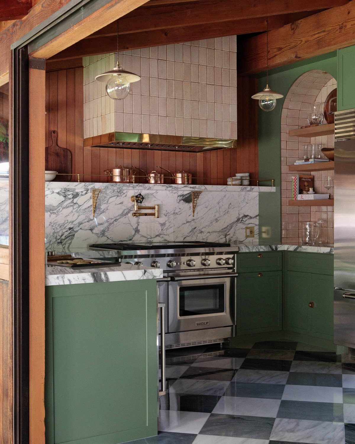 Sage green kitchen cabinets paired with vertical wood paneling and marble countertops.