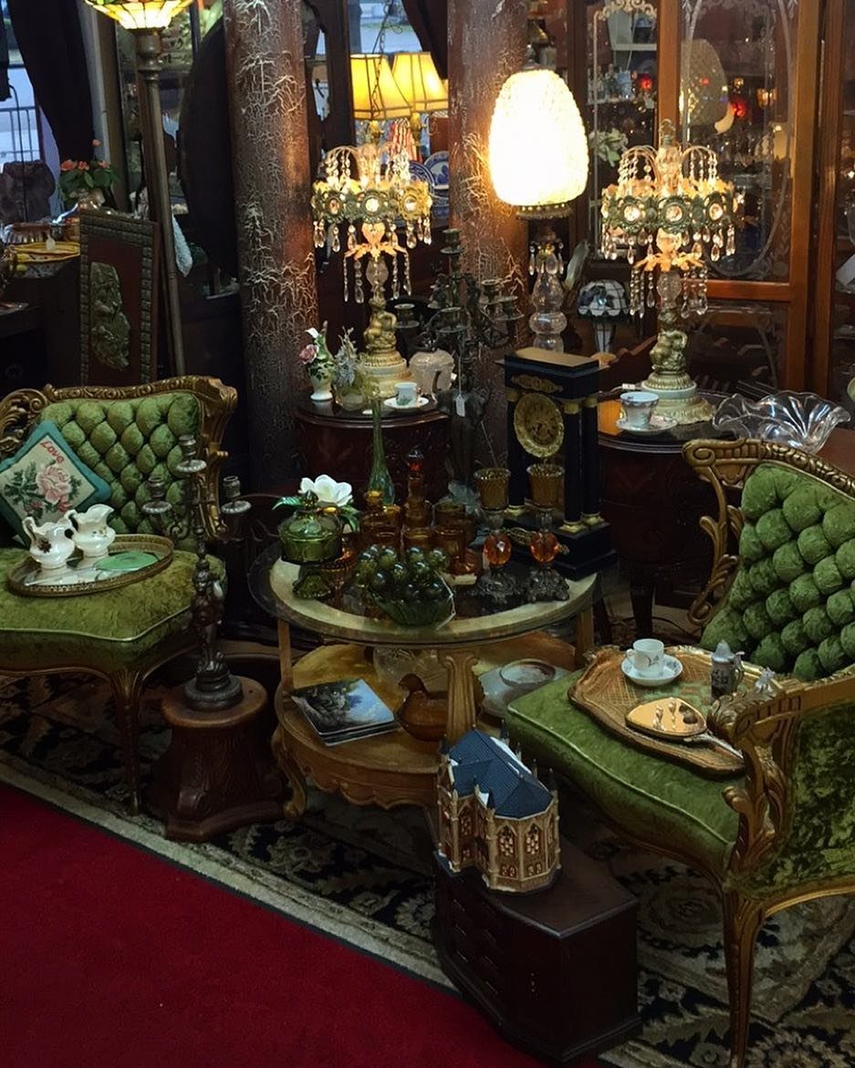 Ornate green velvet chairs and crystal chandeliers surround small antique tables in a shop.