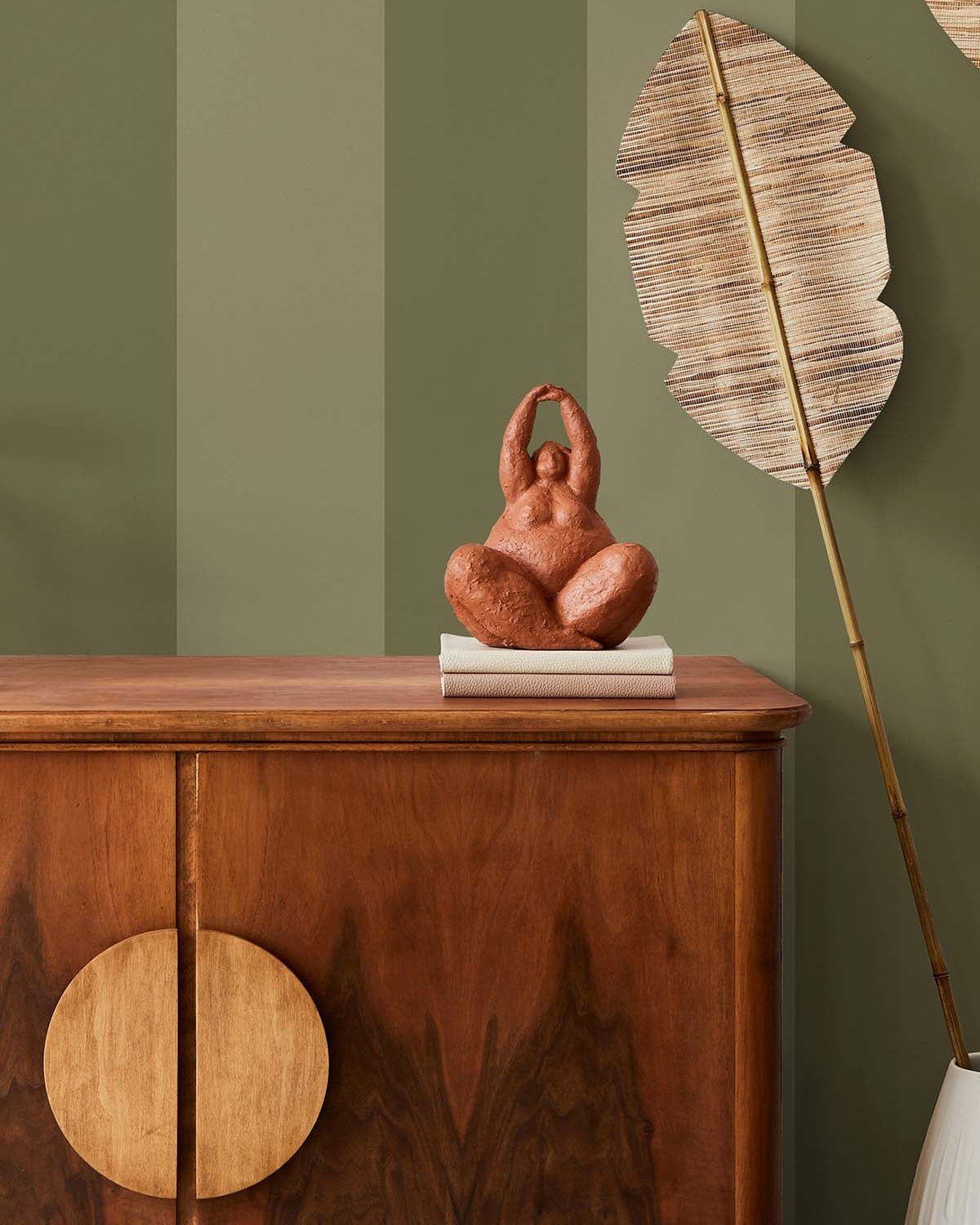 Green striped walls behind a wooden sideboard with a terracotta figurine and woven leaf decor.