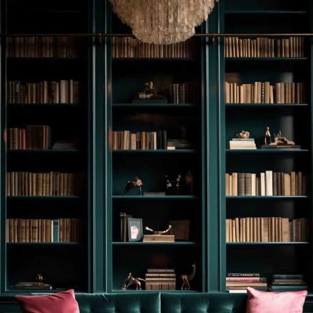 Dark green built-in bookshelves filled with books and decor above a green velvet sofa.