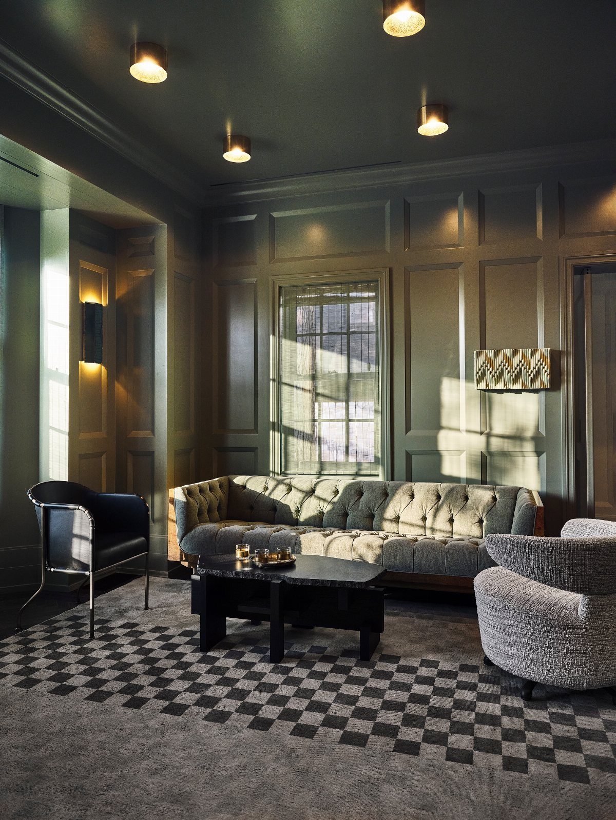 A monochrome living room with gray-green paneled walls, a tufted sofa, and a checkered rug.