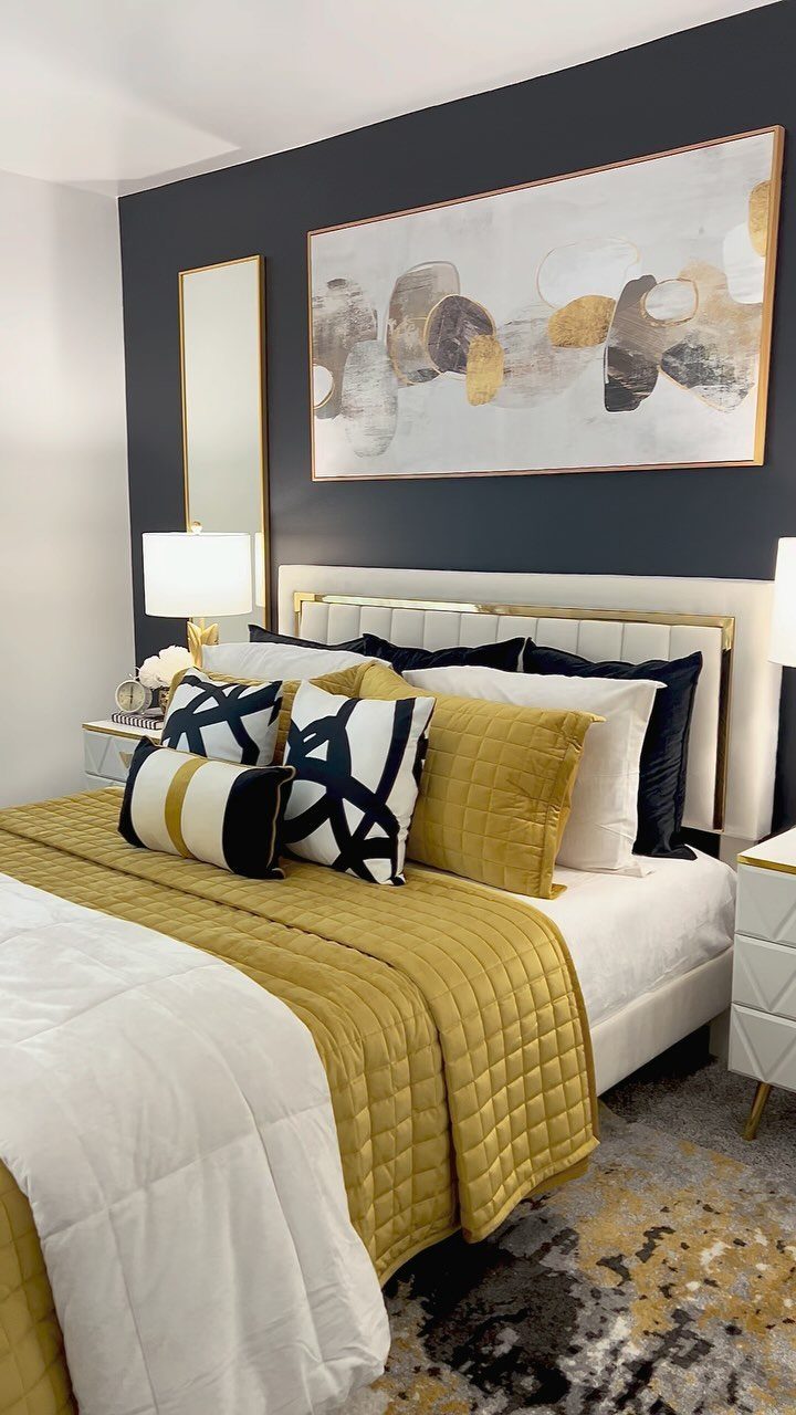 A modern guest bedroom with a gold quilted bedspread, navy and gold pillows, and abstract wall art.