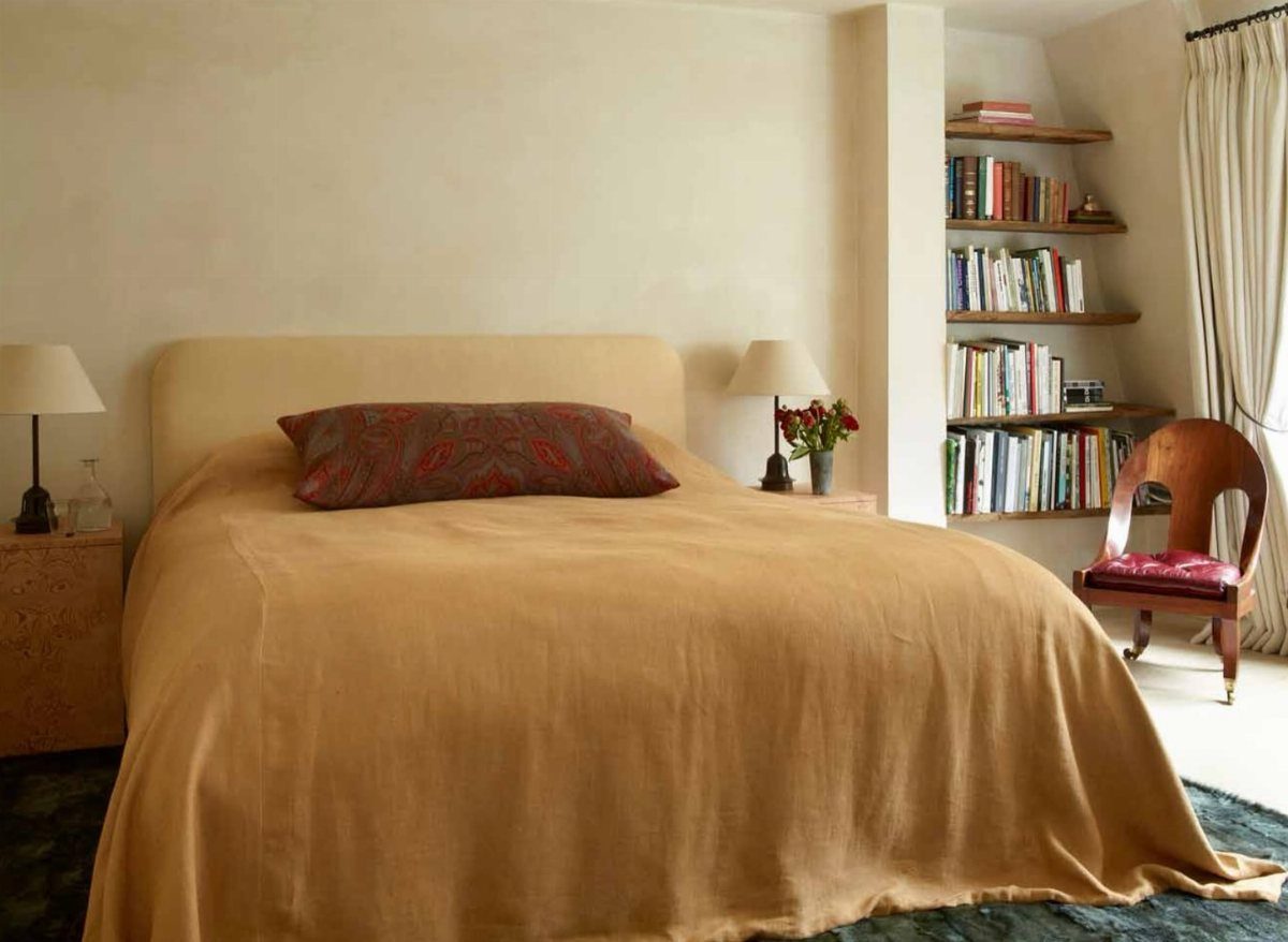 A bed with tan bedding and a patterned pillow sits next to built-in wooden bookshelves.