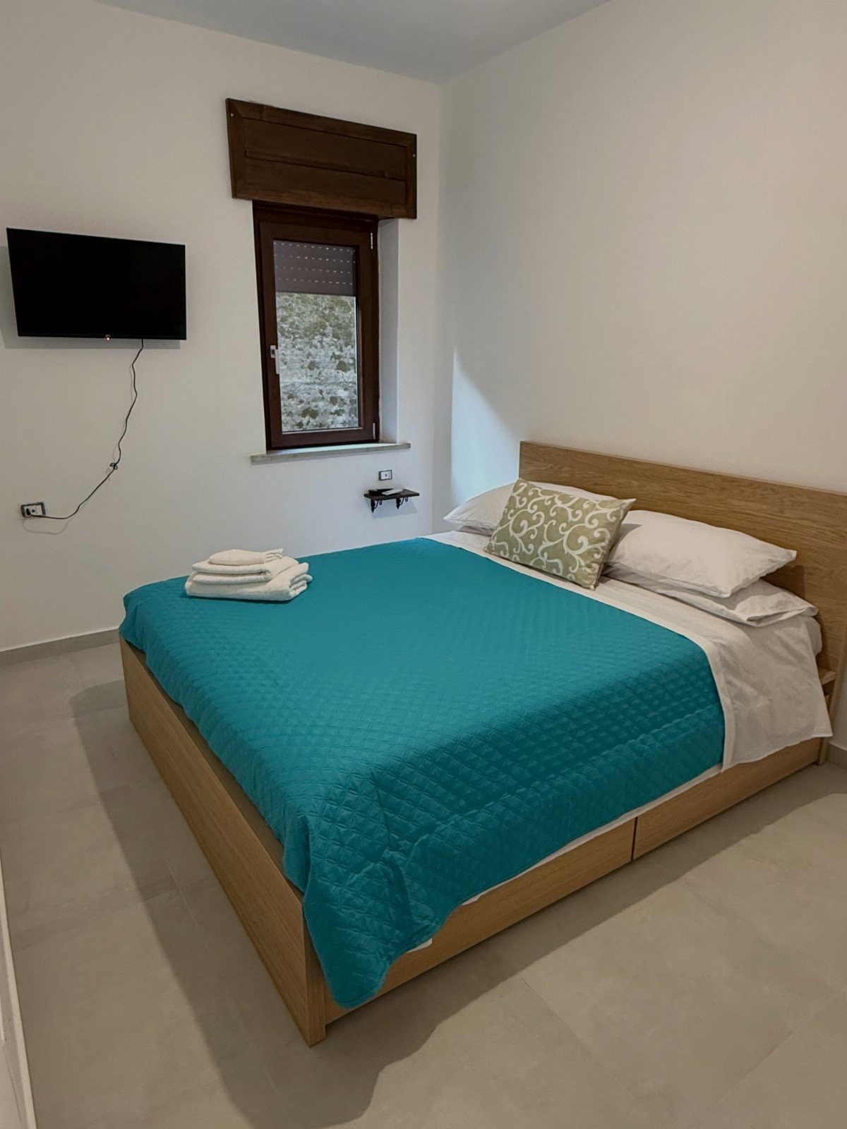 A wooden bed with a turquoise bedspread and a stack of white towels on top.