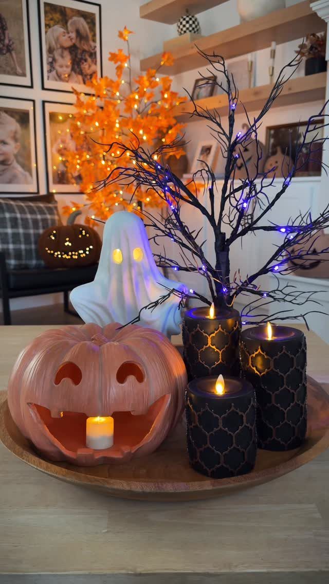 Halloween decorations including a pink pumpkin, ghost, and black candles on a wooden tray.