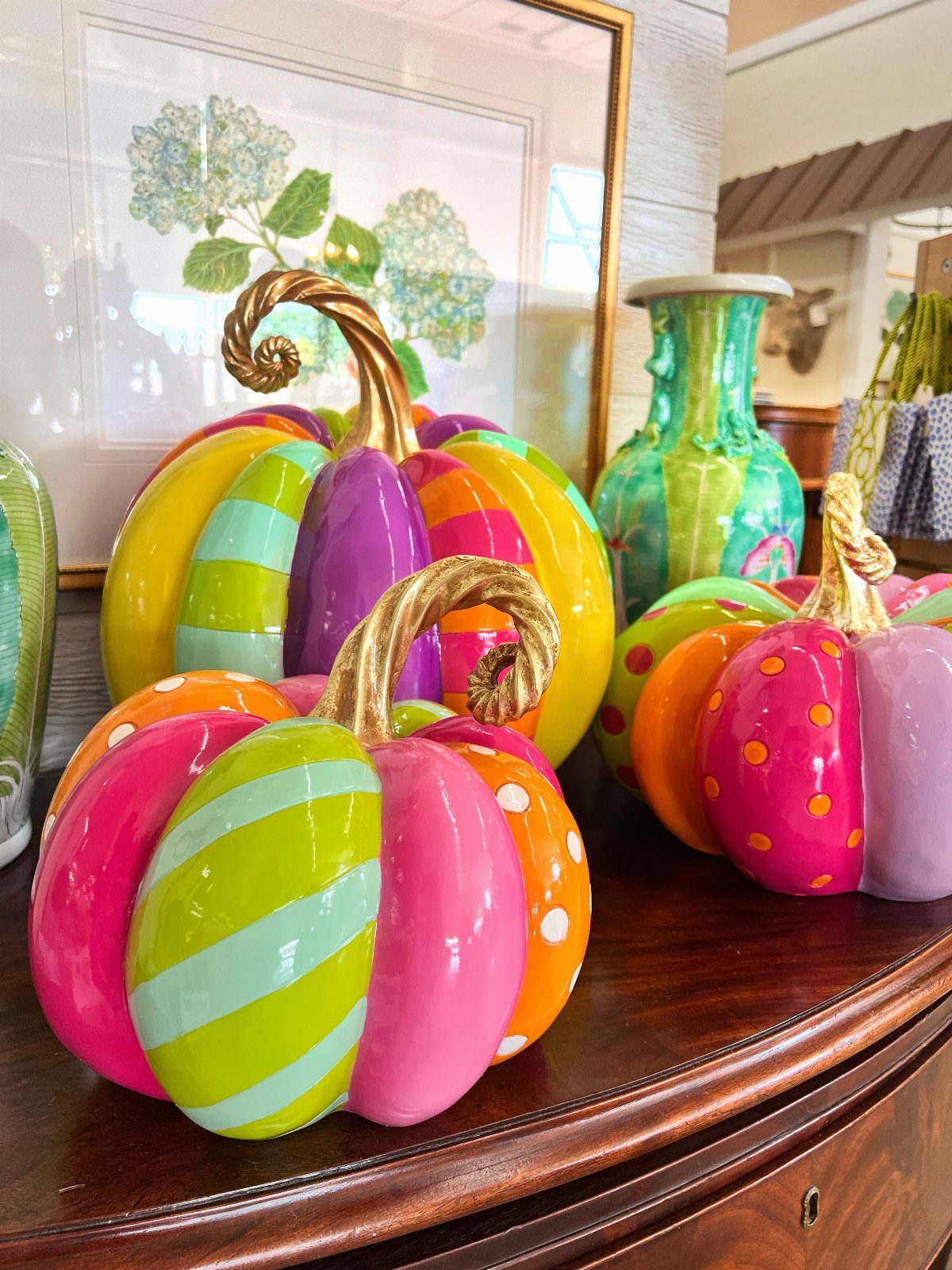 Colorful striped and polka dot ceramic pumpkins resting on a dark wooden dresser.