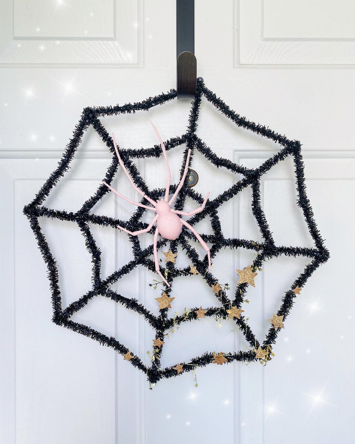 Black tinsel spiderweb with a pink spider and gold stars hanging on a white door.