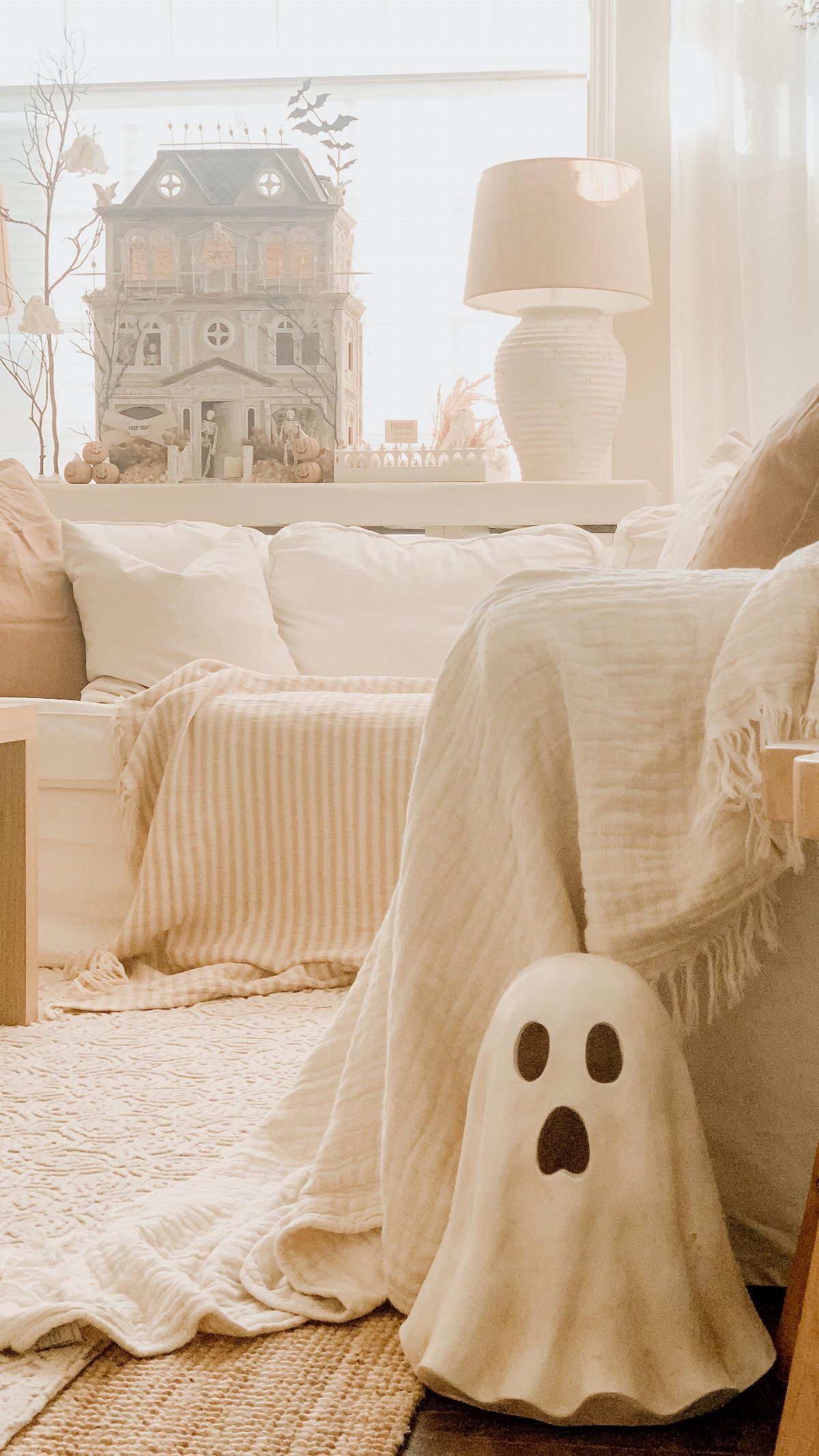 A cream ghost-shaped pillow resting on a textured white blanket in a bright room.