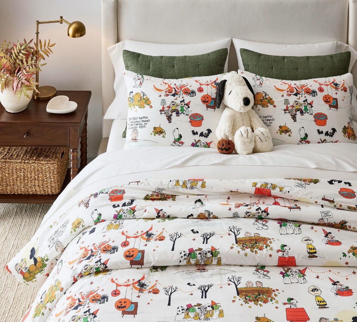 Snoopy themed Halloween bedding on a bed with green pillows and a plush toy.