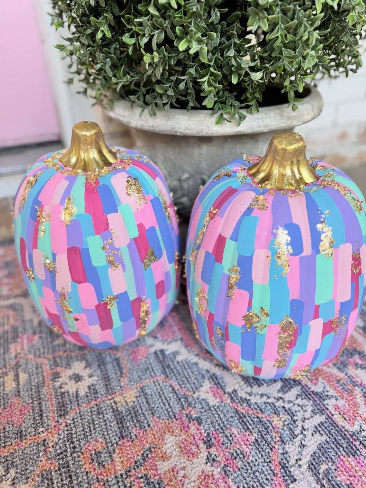 Two pastel-colored striped pumpkins with gold glitter sitting on a patterned rug.
