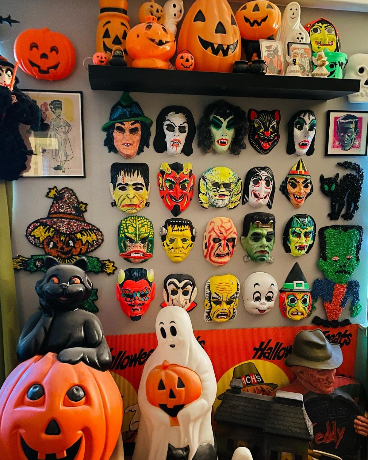 Vintage Halloween masks and plastic jack-o'-lanterns displayed on a shelf and wall.