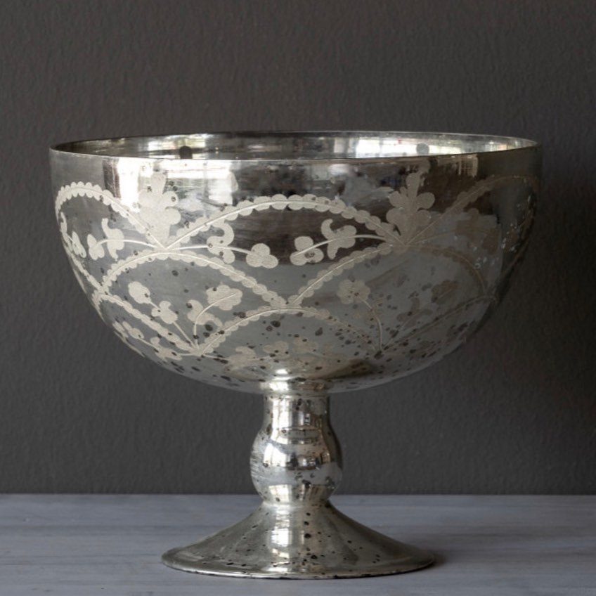 A vintage silver mercury glass pedestal bowl with etched floral patterns on a grey surface.