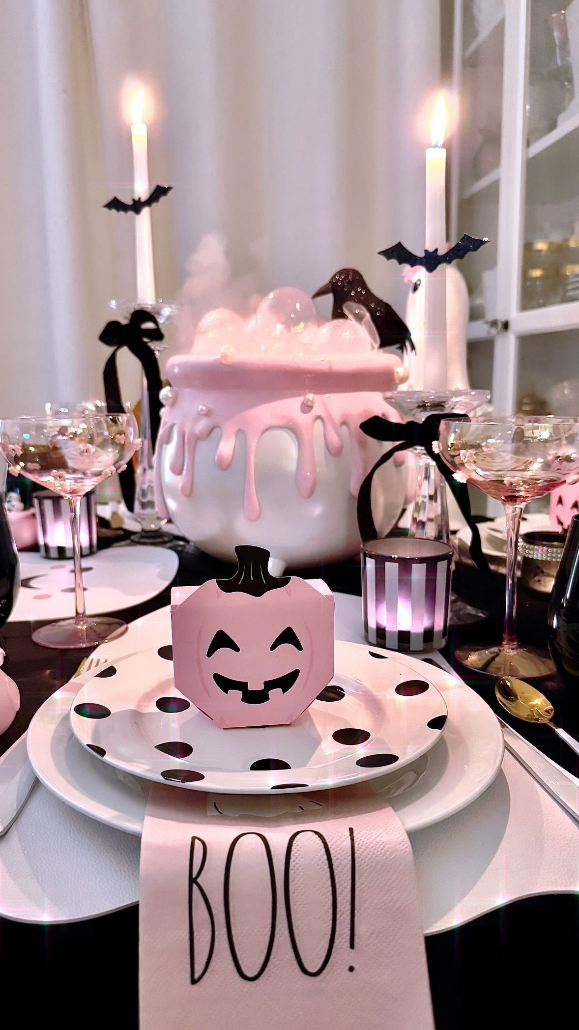 Halloween table setting with pink cauldron, polka dot plates, and candles with bat accents.