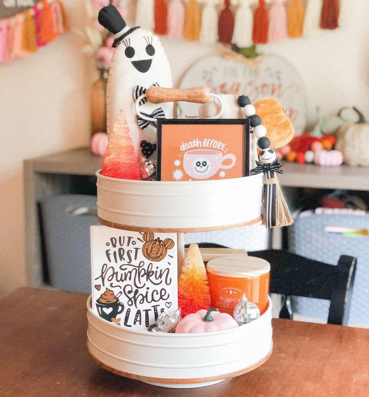 A white two-tiered tray styled with Halloween decorations like a ghost towel and pumpkin signs.