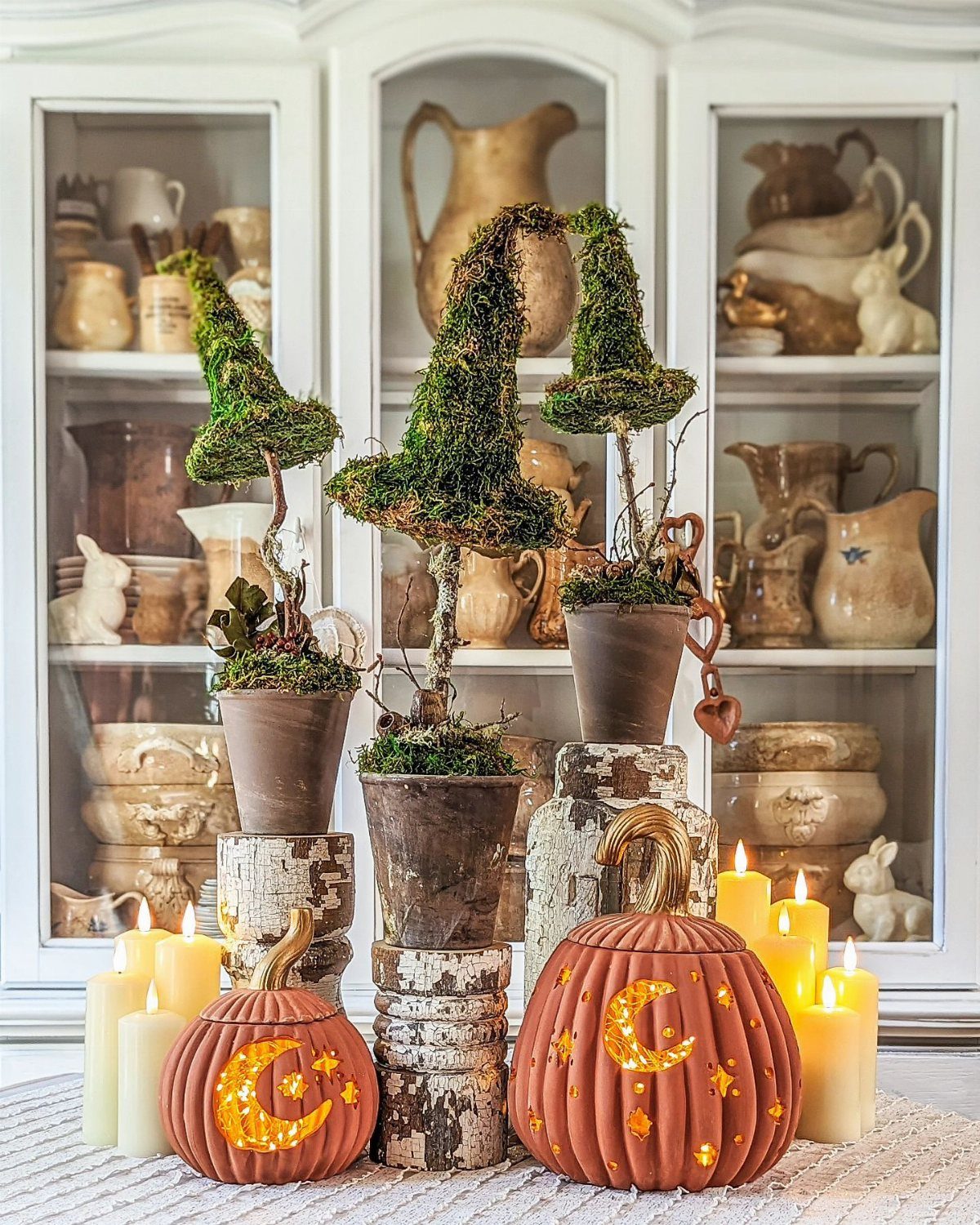 Mossy witch hats in pots and carved glowing pumpkins with candles on a kitchen counter.