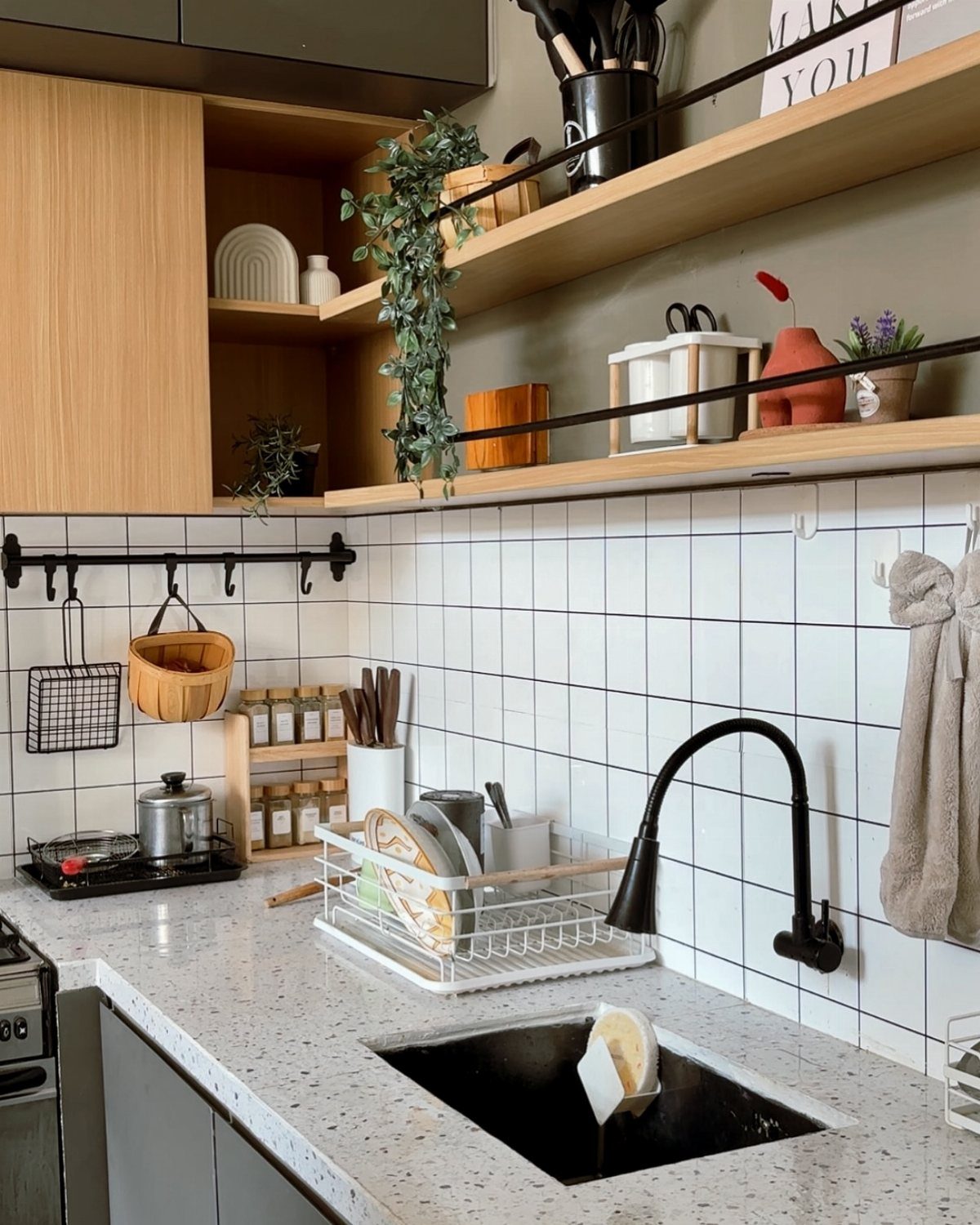 Wooden open shelves with plants and ceramics mounted on a green wall above a kitchen sink.