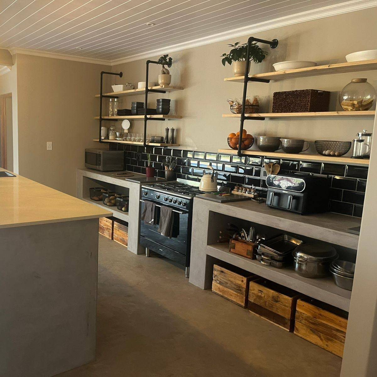 Wooden open kitchen shelves with black industrial metal pipe brackets and various kitchenware.